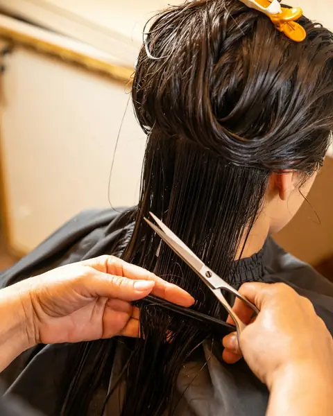 A hairdresser trimming someone&rsquo;s long hair with scissors.
