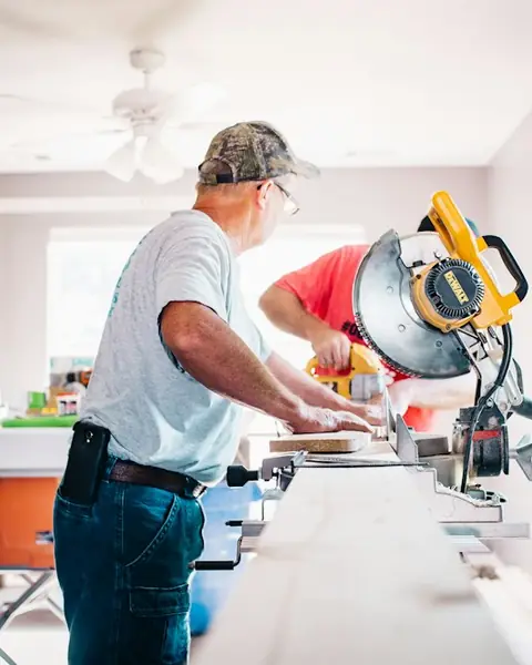 A worker cutting trim on a miter saw during a home renovation.