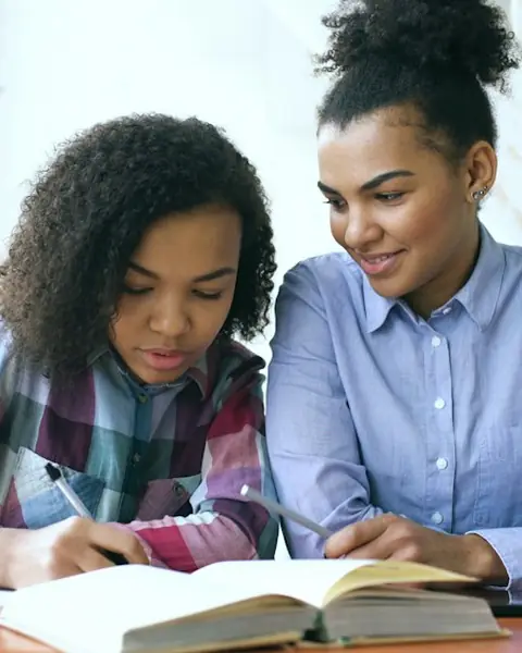 A student working through a lesson with a tutor at a table.